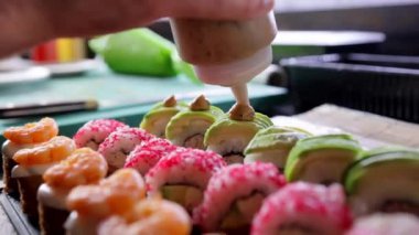 Bir restoranın mutfağında, sos yakın plan çekimde suşinin üzerine serpiştirilir. Suşi hazırlama teknikleri ve aşçılık yaratıcılığı.