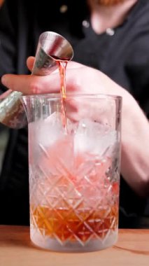 Bir barmen, buzla dolu bir bardağa likör ekleyerek alkollü bir kokteyl hazırlar. Dikey videoyu kapat.