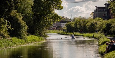 Edinburgh, İngiltere; 05-18-2021: Yazın Union Canal, Harrison Park. Yeşil ağaçlar, çimenlerde oturan arkadaşlar, yürüyen insanlar, kanoda kürek çeken iki kız.