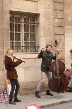 Paris, Fransa. 2/22/15. Le Marais 'de taş kemerlerin, atari salonunun altında, siyah elbiseler, şapkalar ve kırmızı bir eşarp takan bir sokak sanatçısı.