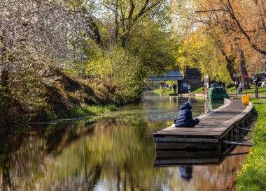 Edinburgh, İskoçya; 04-23-2021: Baharda, Harrison Park 'ın yanındaki Union Kanalı, renkli ağaçlar, yol boyunca insanlar ve rıhtımda oturan bir adam