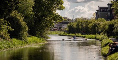 Edinburgh, İngiltere; 05-18-2021: Yazın Union Canal, Harrison Park. Yeşil ağaçlar, çimenlerde oturan arkadaşlar, yürüyen insanlar, kanoda kürek çeken iki kız.