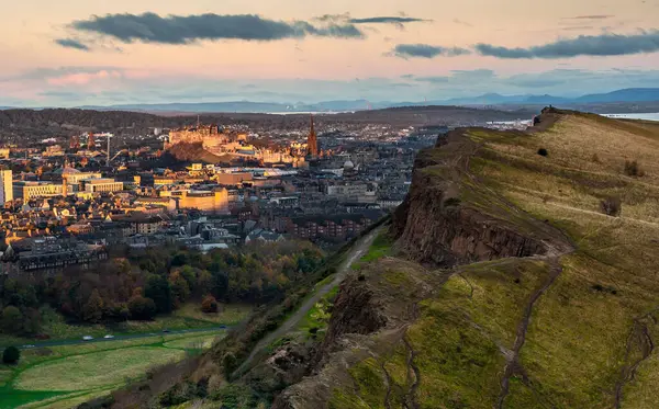 stock image View of the Salisbury Crags from Arthur's Seat at sunrise, with the sun shining on Edinburgh's Castle in the background. Edinburgh, Scotland. Landscape. Cityscape. Travel