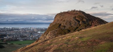 Edinburgh 'daki Arthur Seat Tepesi' nin zirvesine bakın. Tepesinde insanlar ve şehir ve arka planda Forth Firth var.
