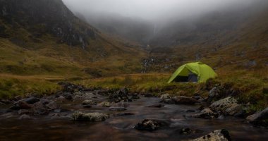 İskoçya 'nın Cairngorms Ulusal Parkı' ndaki Corrie Fee nehrinin yanındaki yeşil bir kamp çadırının manzarası.
