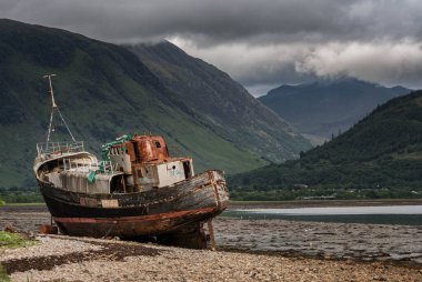 İskoçya 'nın batı kıyısında, Fort William yakınlarında, arkada sis kaplı dağlarla karaya vurmuş bir gemi enkazı.