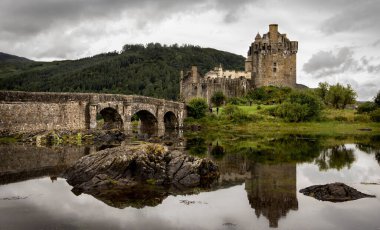 Bulutlu gökyüzü ile Eilean Donan Kalesi 'nin görüntüsü. Köprü ile suya yansıtılıyor. İskoçya