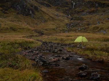 İskoçya 'nın Cairngorms Ulusal Parkı' ndaki Corrie Fee nehrinin yanında yeşil bir kamp çadırı.