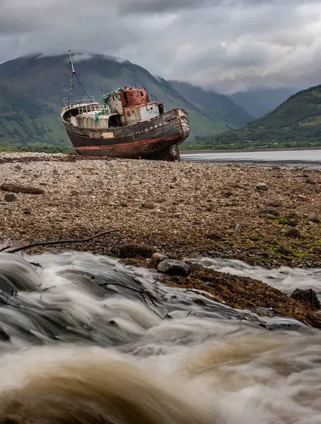 stock image Corpach shipwreck stranded on shore near Fort William, between mountains and a river, in the west coast of Scotland. Vertical