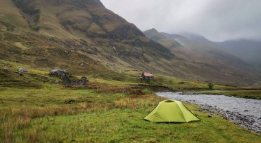 İskoçya 'nın dağlık arazilerindeki Glen Lichd Vadisi' nin yanında yeşil çadır kurmuşlar. Arka planda dağlar ve boz bulutlar varmış. Atmosferik alçak bulutlar.
