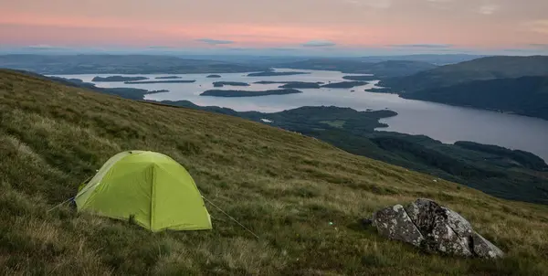 stock image Green tent wild camping on Ben Lomond in the evening, on the slope of the hill overlooking the lake, Loch Lomond and The Trossachs National Park, Scotland