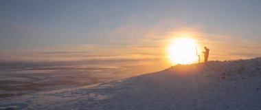 İskoçya 'nın Edinburgh yakınlarındaki Pentlands Hills' te karlı bir tepenin üzerinde duran bir insanın panoramik görüntüsü. Güneş batıyor ve gökyüzü turuncu ve pembe renklerin güzel bir karışımı. Huzurlu ve huzurlu bir sahne.