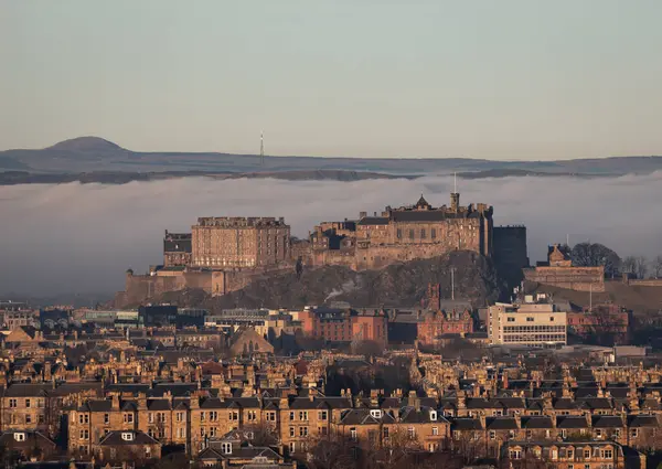 stock image 12.18.2021, Edinburgh, Scotland: Edinburgh Castle with residential buildings in foreground and fog cloud inversion covering the Firth of Forth estuary behind