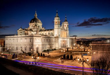 Madrid, İspanya 'daki Almudena Katolik Katedrali' nin gece görüntüsü, mavi saatte aydınlatılmış ve yoldan geçen arabaların mavi ve kırmızı ışıkları açık. Şehirdeki en önemli turistik yerlerden biri.