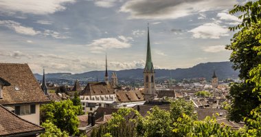 Zürih, İsviçre manzarası, üniversitedeki Polyterrasse 'den kilise kulesine, arka plandaki dağlara, öndeki ağaçlara ve mavi gökyüzündeki bulutlara