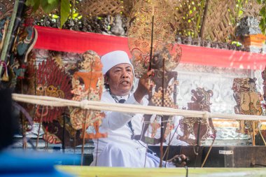 Geleneksel kıyafetler giymiş Balili adam gölge kukla gösterisi oynuyor (wayang kulit)).