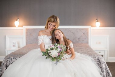 Düğün için. Evdeki gibi beyaz stüdyo içinde, güzel elbiseli gelin kanepede oturuyor. Modaya uygun bir düğün fotoğrafı. Genç, beyaz, esmer bir model, gelin gibi.