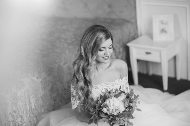 Düğün için. Evdeki gibi beyaz stüdyo içinde, güzel elbiseli gelin kanepede oturuyor. Modaya uygun bir düğün fotoğrafı. Genç, beyaz, esmer bir model, gelin gibi.