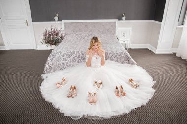 Düğün için. Evdeki gibi beyaz stüdyo içinde, güzel elbiseli gelin kanepede oturuyor. Modaya uygun bir düğün fotoğrafı. Genç, beyaz, esmer bir model, gelin gibi.