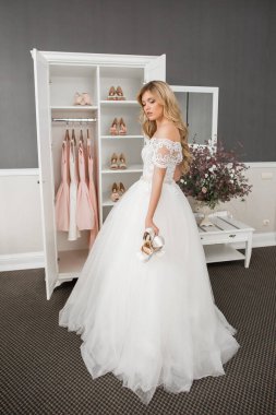 Düğün için. Evdeki gibi beyaz stüdyo içinde, güzel elbiseli gelin kanepede oturuyor. Modaya uygun bir düğün fotoğrafı. Genç, beyaz, esmer bir model, gelin gibi.