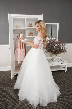 Düğün için. Evdeki gibi beyaz stüdyo içinde, güzel elbiseli gelin kanepede oturuyor. Modaya uygun bir düğün fotoğrafı. Genç, beyaz, esmer bir model, gelin gibi.