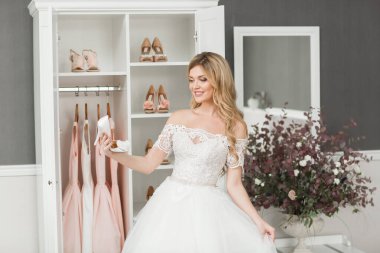Düğün için. Evdeki gibi beyaz stüdyo içinde, güzel elbiseli gelin kanepede oturuyor. Modaya uygun bir düğün fotoğrafı. Genç, beyaz, esmer bir model, gelin gibi.