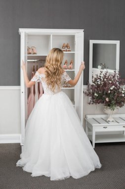 Düğün için. Evdeki gibi beyaz stüdyo içinde, güzel elbiseli gelin kanepede oturuyor. Modaya uygun bir düğün fotoğrafı. Genç, beyaz, esmer bir model, gelin gibi.