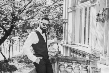 Açık mavi takım elbiseli yakışıklı Çinli genç bir adamın portresi ve beyaz atlet, güneşli bir günde modern şehir binalarıyla yürüyor ve uzaklara bakıyor, kendinden emin iş adamının yan görünüşü..