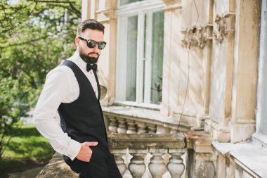 Açık mavi takım elbiseli yakışıklı Çinli genç bir adamın portresi ve beyaz atlet, güneşli bir günde modern şehir binalarıyla yürüyor ve uzaklara bakıyor, kendinden emin iş adamının yan görünüşü..