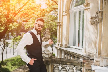 Açık mavi takım elbiseli yakışıklı Çinli genç bir adamın portresi ve beyaz atlet, güneşli bir günde modern şehir binalarıyla yürüyor ve uzaklara bakıyor, kendinden emin iş adamının yan görünüşü..