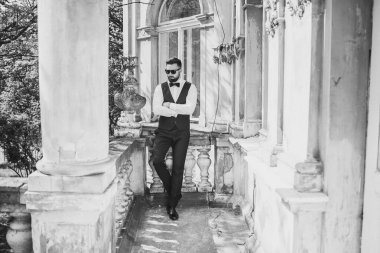 Açık mavi takım elbiseli yakışıklı Çinli genç bir adamın portresi ve beyaz atlet, güneşli bir günde modern şehir binalarıyla yürüyor ve uzaklara bakıyor, kendinden emin iş adamının yan görünüşü..