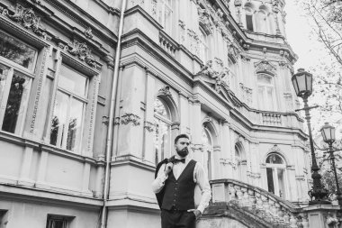 Açık mavi takım elbiseli yakışıklı Çinli genç bir adamın portresi ve beyaz atlet, güneşli bir günde modern şehir binalarıyla yürüyor ve uzaklara bakıyor, kendinden emin iş adamının yan görünüşü..