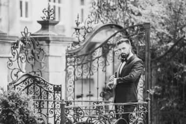 Açık mavi takım elbiseli yakışıklı Çinli genç bir adamın portresi ve beyaz atlet, güneşli bir günde modern şehir binalarıyla yürüyor ve uzaklara bakıyor, kendinden emin iş adamının yan görünüşü..