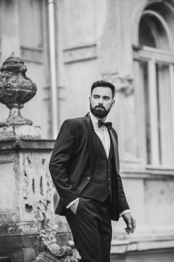 Açık mavi takım elbiseli yakışıklı Çinli genç bir adamın portresi ve beyaz atlet, güneşli bir günde modern şehir binalarıyla yürüyor ve uzaklara bakıyor, kendinden emin iş adamının yan görünüşü..