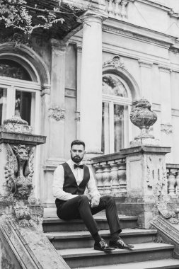 Açık mavi takım elbiseli yakışıklı Çinli genç bir adamın portresi ve beyaz atlet, güneşli bir günde modern şehir binalarıyla yürüyor ve uzaklara bakıyor, kendinden emin iş adamının yan görünüşü..