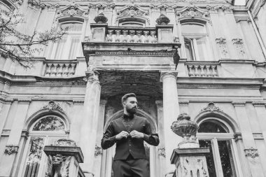 Açık mavi takım elbiseli yakışıklı Çinli genç bir adamın portresi ve beyaz atlet, güneşli bir günde modern şehir binalarıyla yürüyor ve uzaklara bakıyor, kendinden emin iş adamının yan görünüşü..