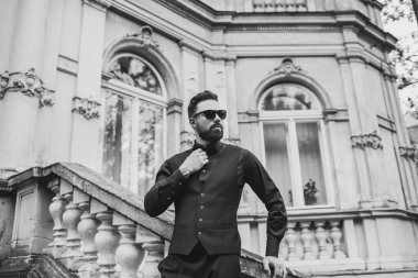 Açık mavi takım elbiseli yakışıklı Çinli genç bir adamın portresi ve beyaz atlet, güneşli bir günde modern şehir binalarıyla yürüyor ve uzaklara bakıyor, kendinden emin iş adamının yan görünüşü..