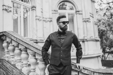 Açık mavi takım elbiseli yakışıklı Çinli genç bir adamın portresi ve beyaz atlet, güneşli bir günde modern şehir binalarıyla yürüyor ve uzaklara bakıyor, kendinden emin iş adamının yan görünüşü..