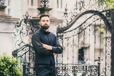 Açık mavi takım elbiseli yakışıklı Çinli genç bir adamın portresi ve beyaz atlet, güneşli bir günde modern şehir binalarıyla yürüyor ve uzaklara bakıyor, kendinden emin iş adamının yan görünüşü..