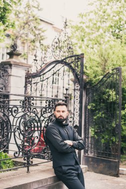 Açık mavi takım elbiseli yakışıklı Çinli genç bir adamın portresi ve beyaz atlet, güneşli bir günde modern şehir binalarıyla yürüyor ve uzaklara bakıyor, kendinden emin iş adamının yan görünüşü..