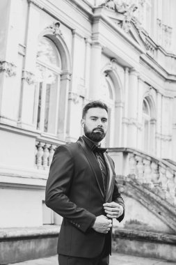 Açık mavi takım elbiseli yakışıklı Çinli genç bir adamın portresi ve beyaz atlet, güneşli bir günde modern şehir binalarıyla yürüyor ve uzaklara bakıyor, kendinden emin iş adamının yan görünüşü..