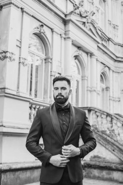 Açık mavi takım elbiseli yakışıklı Çinli genç bir adamın portresi ve beyaz atlet, güneşli bir günde modern şehir binalarıyla yürüyor ve uzaklara bakıyor, kendinden emin iş adamının yan görünüşü..