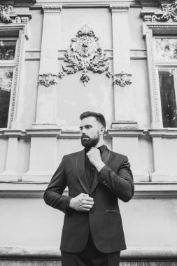 Açık mavi takım elbiseli yakışıklı Çinli genç bir adamın portresi ve beyaz atlet, güneşli bir günde modern şehir binalarıyla yürüyor ve uzaklara bakıyor, kendinden emin iş adamının yan görünüşü..