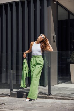 Zarif, kendine güvenen, modaya uygun pembe güneş gözlüğü takan, ipek başörtüsü takan, yeşil çantalı, Avrupa sokaklarında poz veren zarif bir kadın. Açık hava moda portresi. Kopyala, metin için boşluk