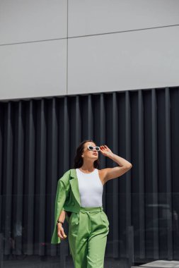 Zarif, kendine güvenen, modaya uygun pembe güneş gözlüğü takan, ipek başörtüsü takan, yeşil çantalı, Avrupa sokaklarında poz veren zarif bir kadın. Açık hava moda portresi. Kopyala, metin için boşluk
