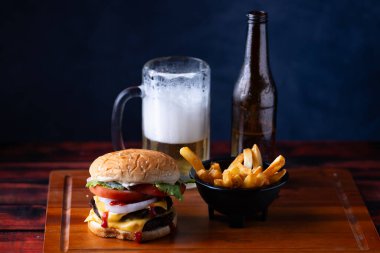 Peynir, marul, domates ve baharatlarla dolu doyurucu bir hamburger gevrek bir yemek atmosferinde soğuk bir şişe birayla birlikte kızarmış patates servisinin yanında oturur..