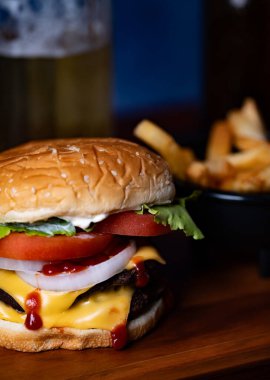 A mouthwatering cheeseburger stacked with lettuce, tomato, onions, and sauce sits next to a portion of crispy fries and a cold drink in a relaxed dining environment. clipart