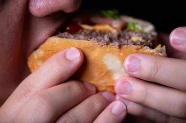 A person is about to take a big bite of a hamburger filled with ground beef, lettuce, and condiments. This moment captures the joy of casual dining during midday. clipart