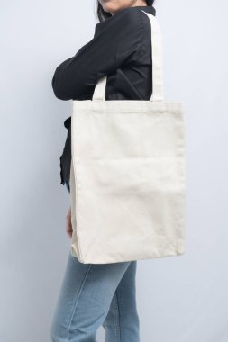 Siyah tişörtlü ve kot pantolonlu biri tarafından tutulan sade beyaz bir çanta.