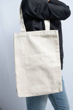 A plain white tote bag held by a person in a black shirt and blue jeans clipart